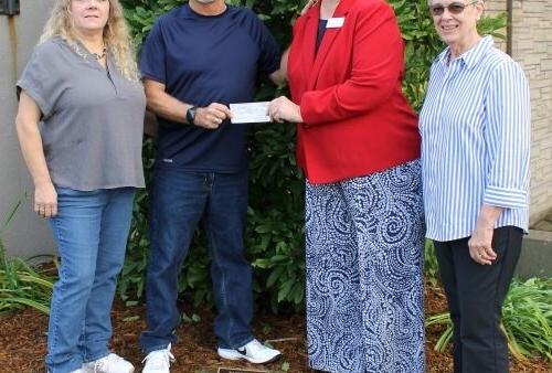 4 people standing outdoors with a check